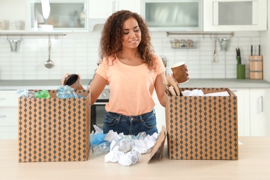 Photo of Young African-American woman sorting garbage in kitchen. Recycling concept