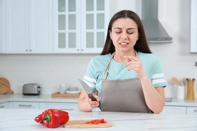 Photo of Woman cut finger with knife while cooking in kitchen