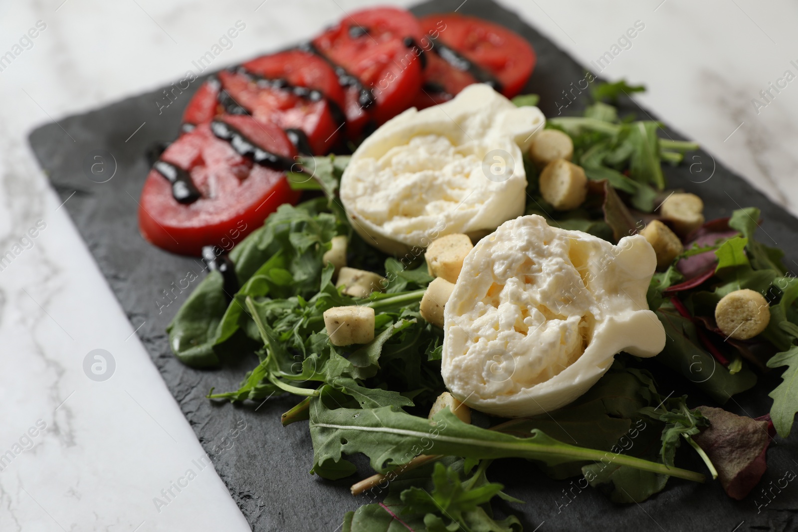 Photo of Delicious burrata cheese, tomatoes and arugula on white marble table, closeup