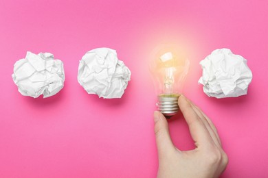 Photo of Woman holding lightbulb among paper balls on pink background, top view. Idea concept