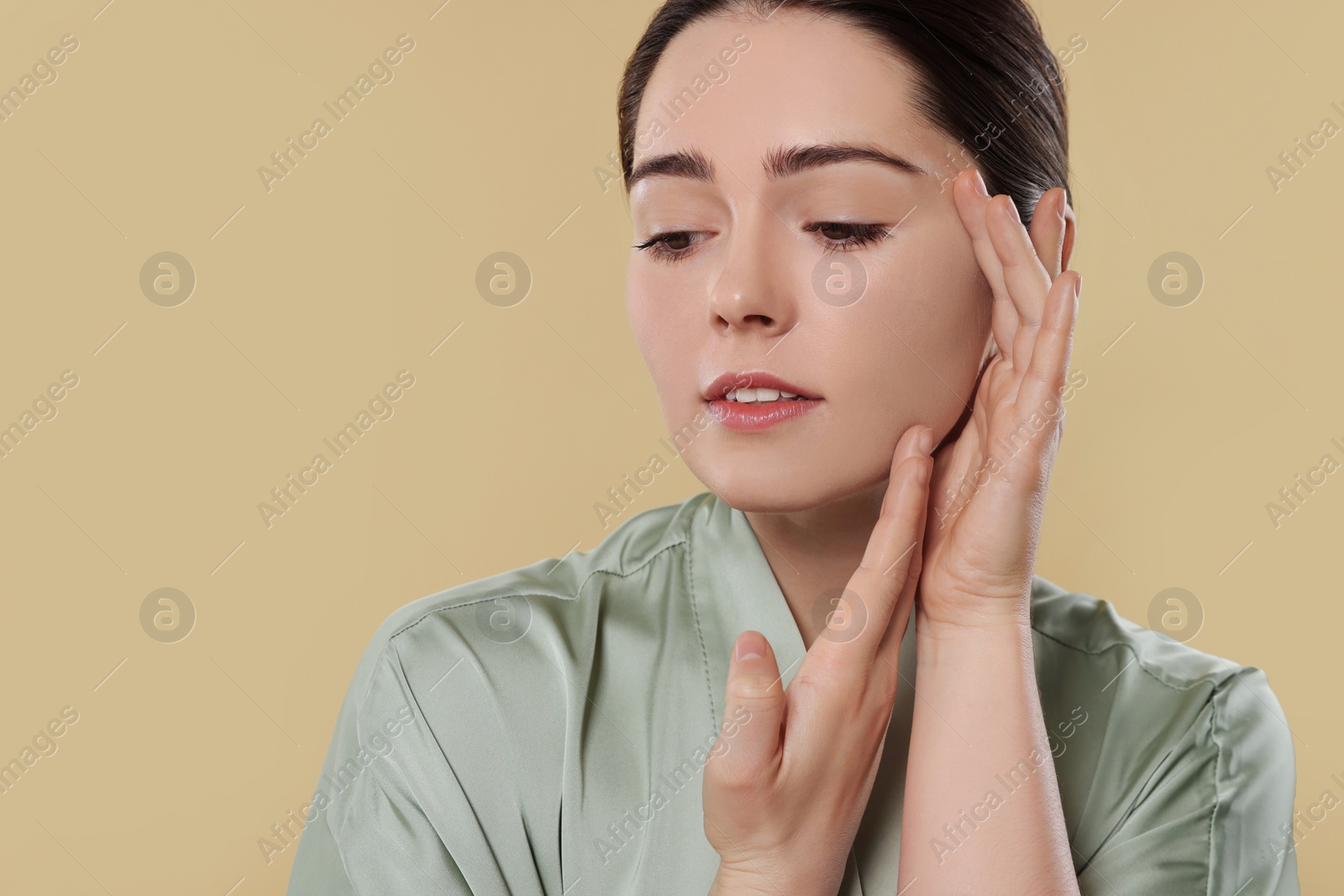 Photo of Young woman massaging her face on beige background. Space for text