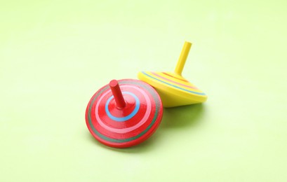 Photo of Two bright spinning tops on light green background, closeup. Toy whirligig