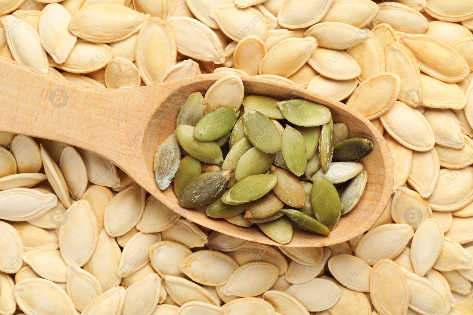 Photo of Wooden spoon on pumpkin seeds, top view