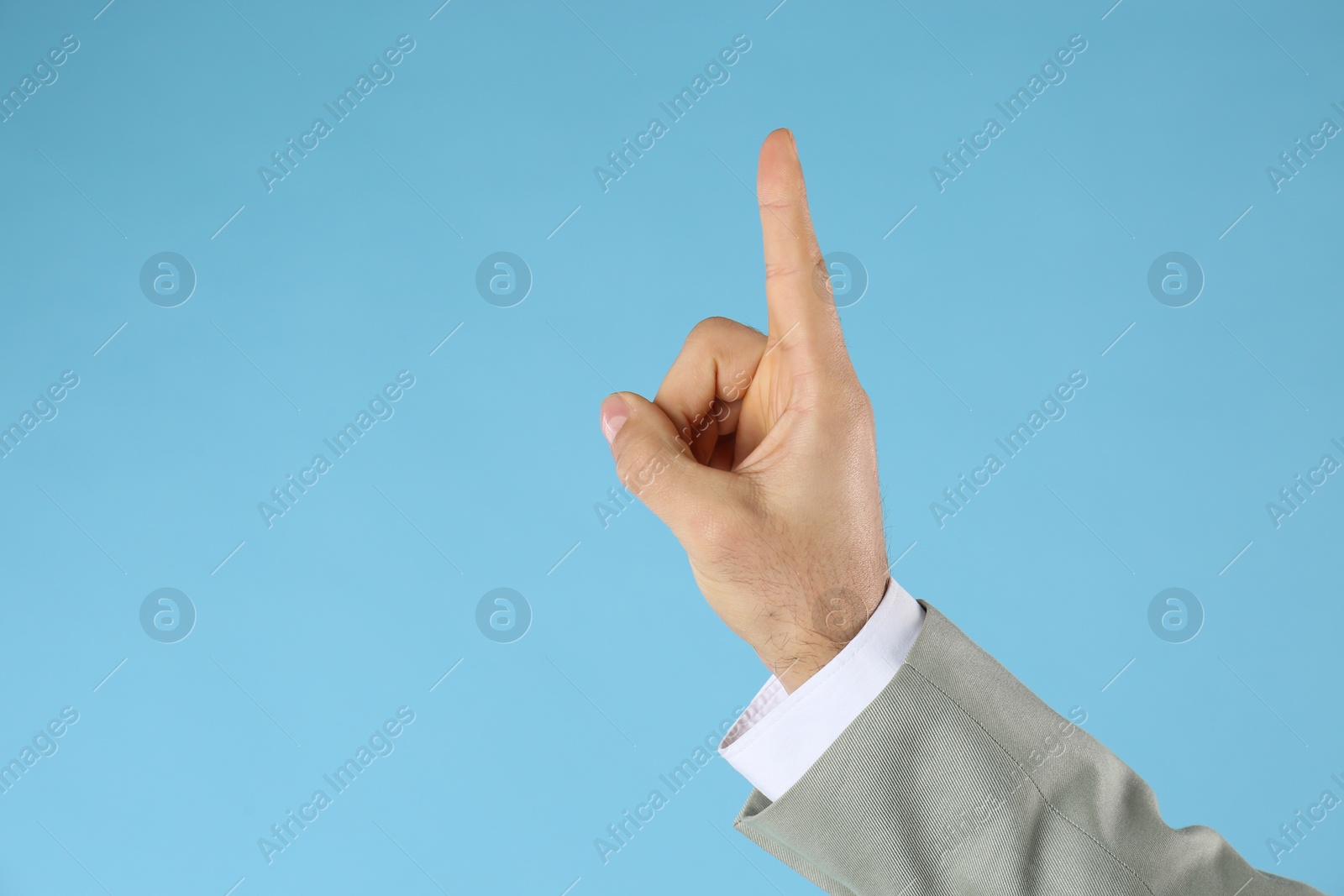 Photo of Businessman pointing at something on light blue background, closeup. Finger gesture