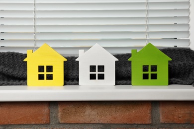 Photo of Different house models on windowsill indoors. Heating efficiency