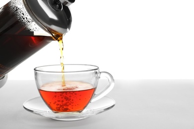 Pouring hot tea into glass cup on white background