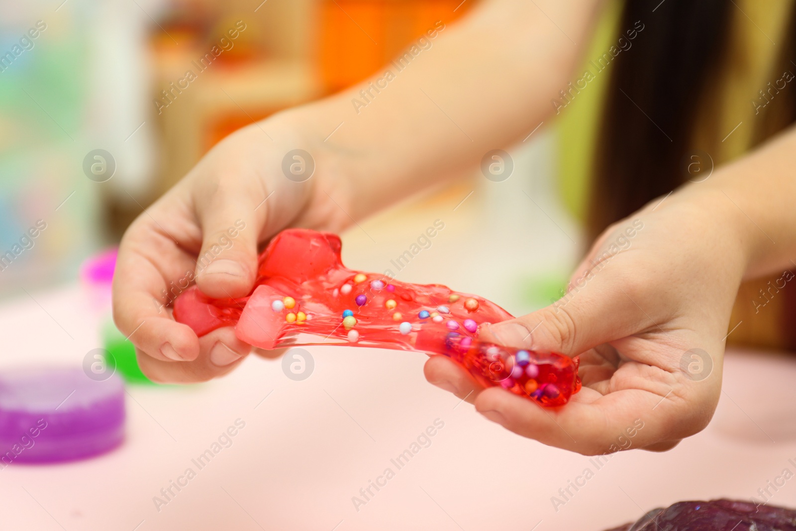 Photo of Little girl playing with red slime indoors, closeup