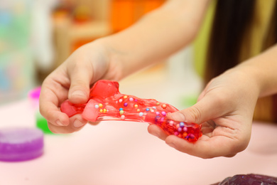 Little girl playing with red slime indoors, closeup