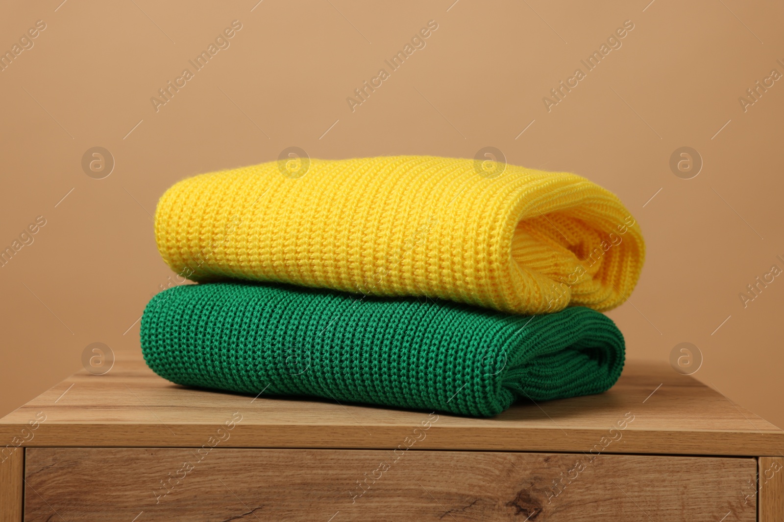 Photo of Stack of knitted sweaters on wooden table against light brown background