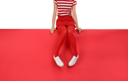 Woman wearing red tights and stylish shoes sitting on color background, closeup