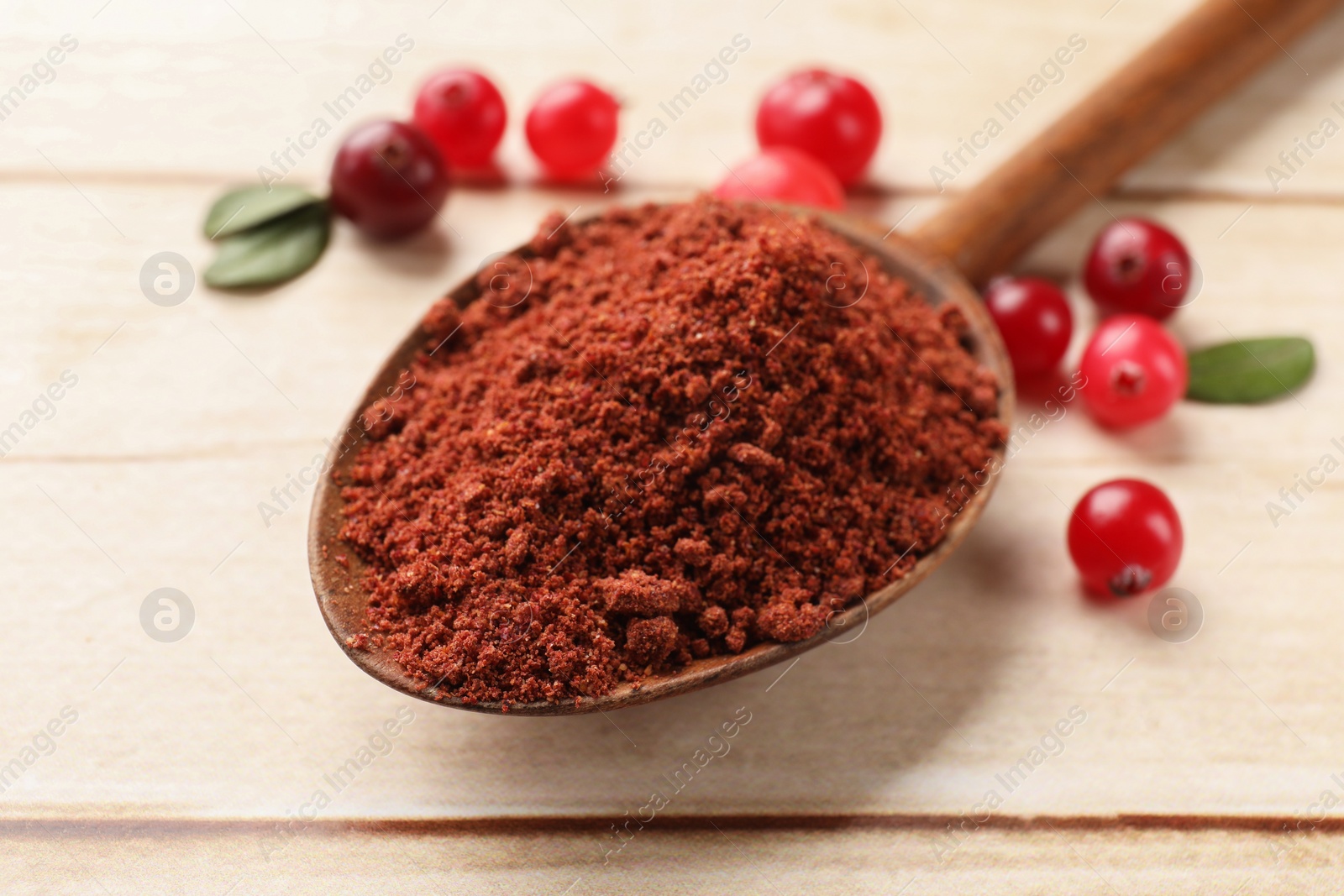 Photo of Dried cranberry powder in spoon, fresh berries and green leaves on light wooden table, closeup