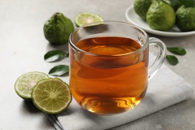 Photo of Glass cup of tasty bergamot tea and fresh fruits on light grey table, closeup
