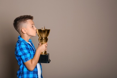 Photo of Happy boy kissing golden winning cup on beige background. Space for text