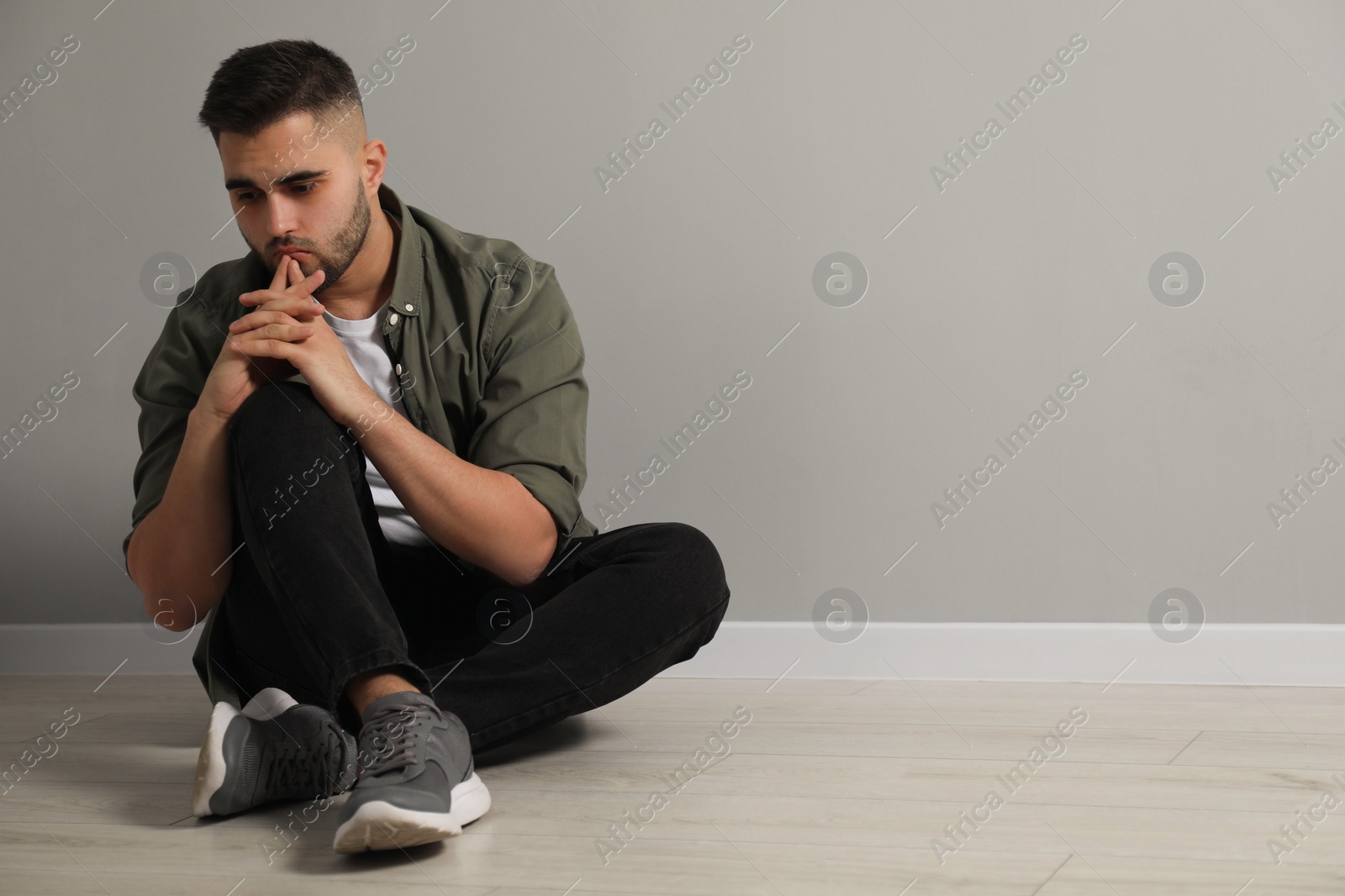 Photo of Sad man sitting on floor near light grey wall. Space for text