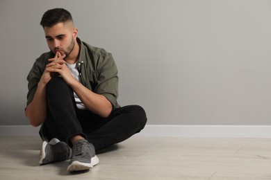 Sad man sitting on floor near light grey wall. Space for text