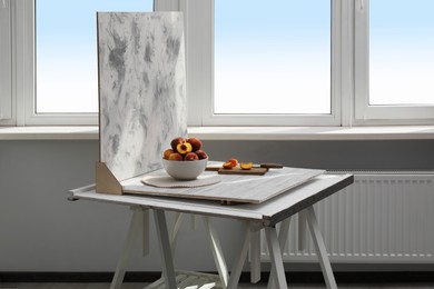 Bowl of juicy peaches and double-sided backdrop on table in photo studio