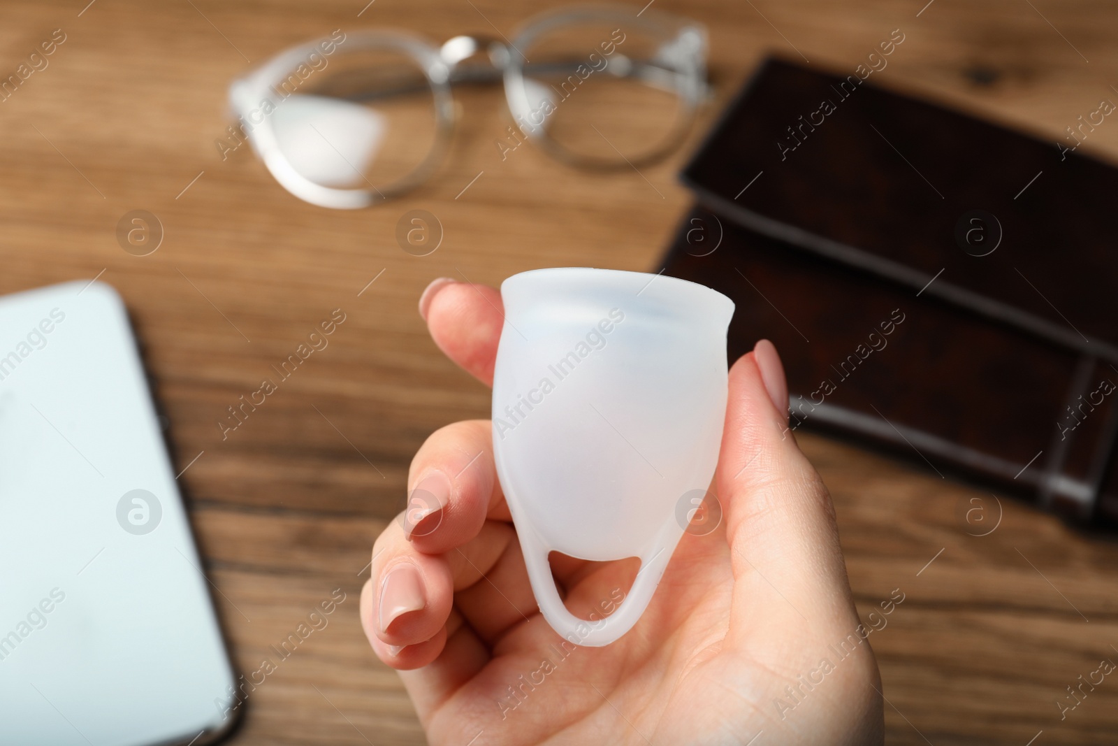 Photo of Woman holding white menstrual cup over wooden table, closeup