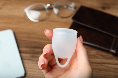 Woman holding white menstrual cup over wooden table, closeup