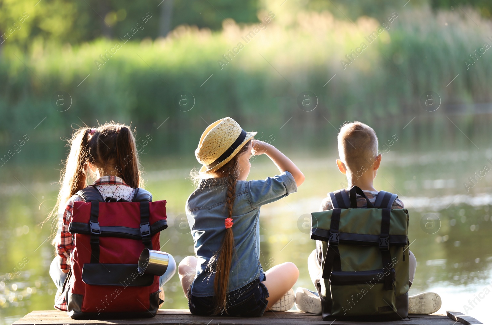 Photo of Little children sitting on wooden pier. Summer camp