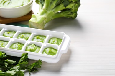 Photo of Broccoli puree in ice cube tray and ingredients on white wooden table, space for text. Ready for freezing
