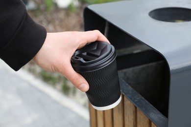 Photo of Man throwing black paper cup into trash can outdoors, closeup