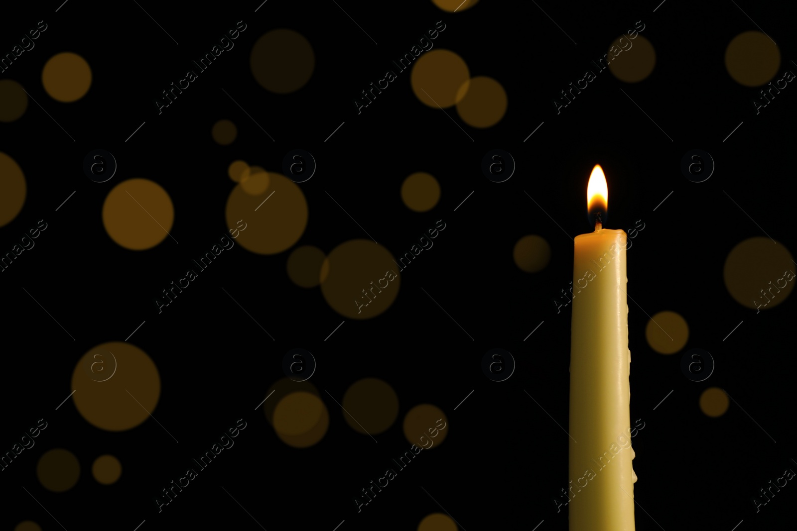 Photo of Wax candle burning against blurred lights in darkness, closeup. Space for text