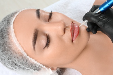 Photo of Young woman getting permanent makeup on lips in beautician salon, closeup