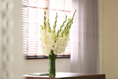 Vase with beautiful white gladiolus flowers on wooden table in room, space for text