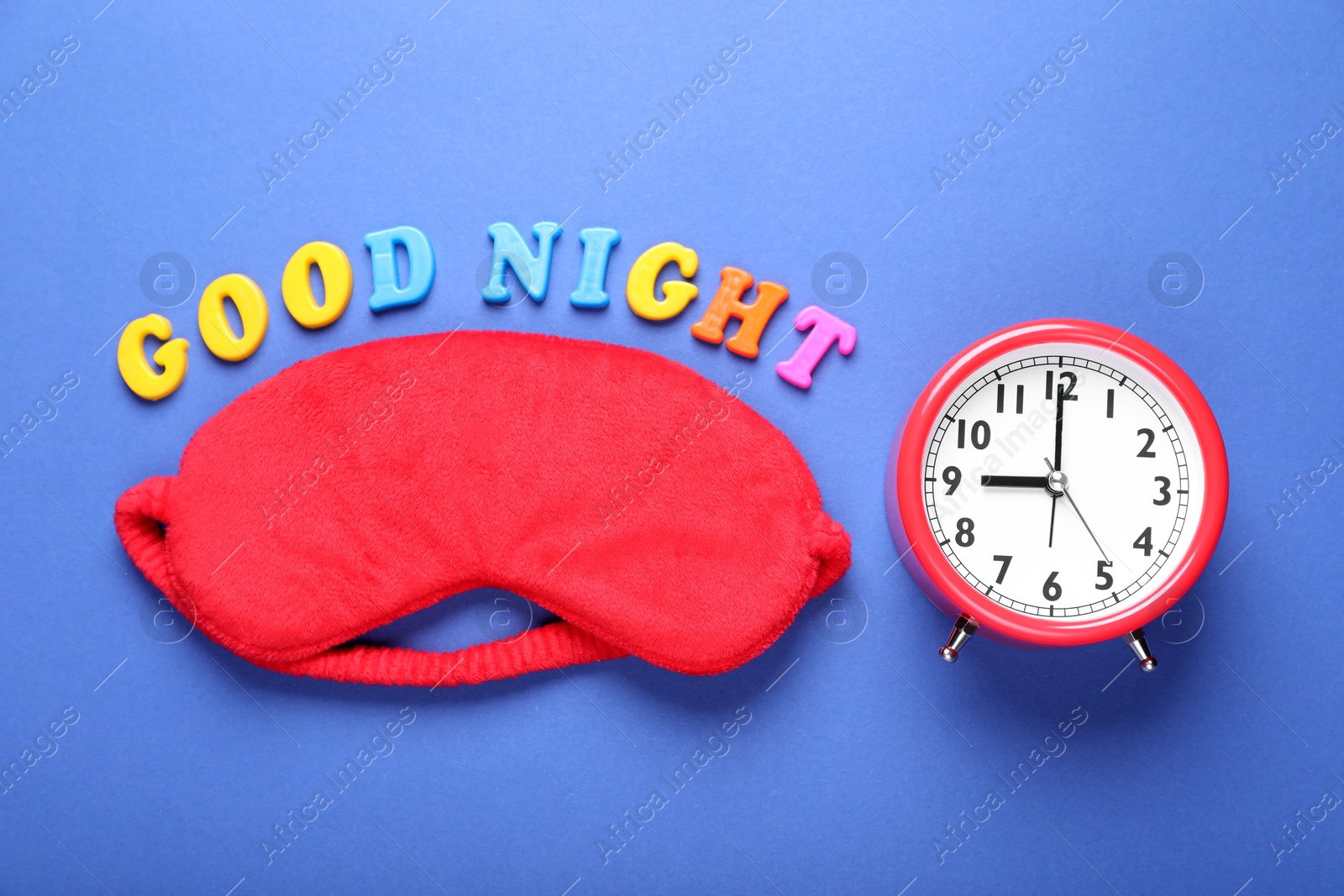 Photo of Soft sleep mask, alarm clock and words Good Night made of colorful letters on blue background, flat lay