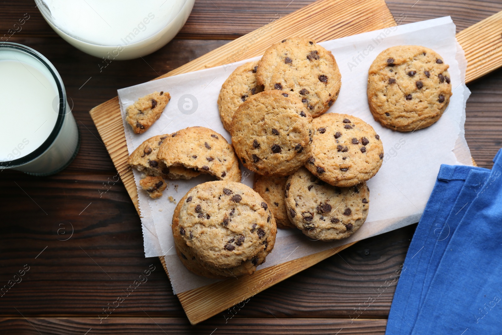 Photo of Delicious chocolate chip cookies and milk on wooden table, flat lay