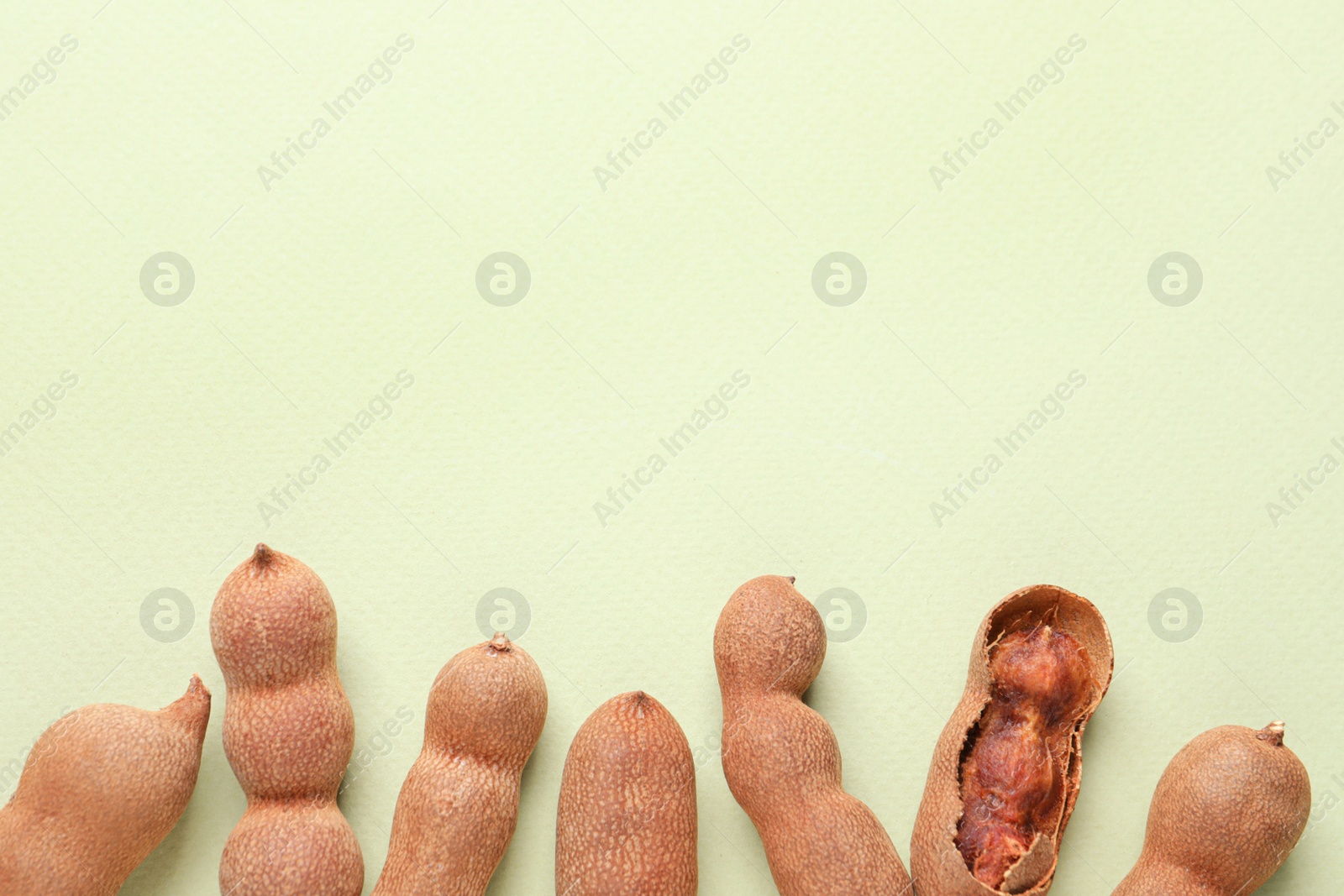 Photo of Ripe tamarinds on light green background, flat lay. Space for text