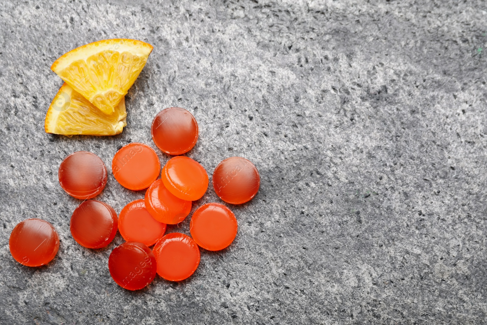 Photo of Many cough drops and slices of orange on grey background, flat lay. Space for text