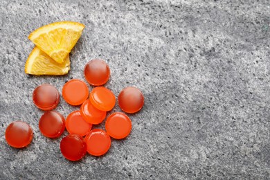 Many cough drops and slices of orange on grey background, flat lay. Space for text