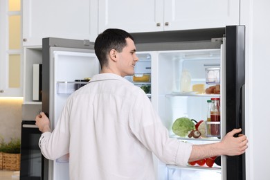 Happy man near refrigerator in kitchen at home, back view