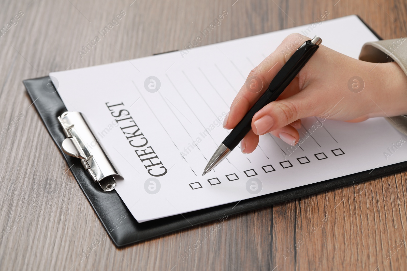 Photo of Woman filling Checklist at wooden table, closeup