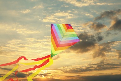 Image of Bright striped rainbow kite flying in sky at sunset