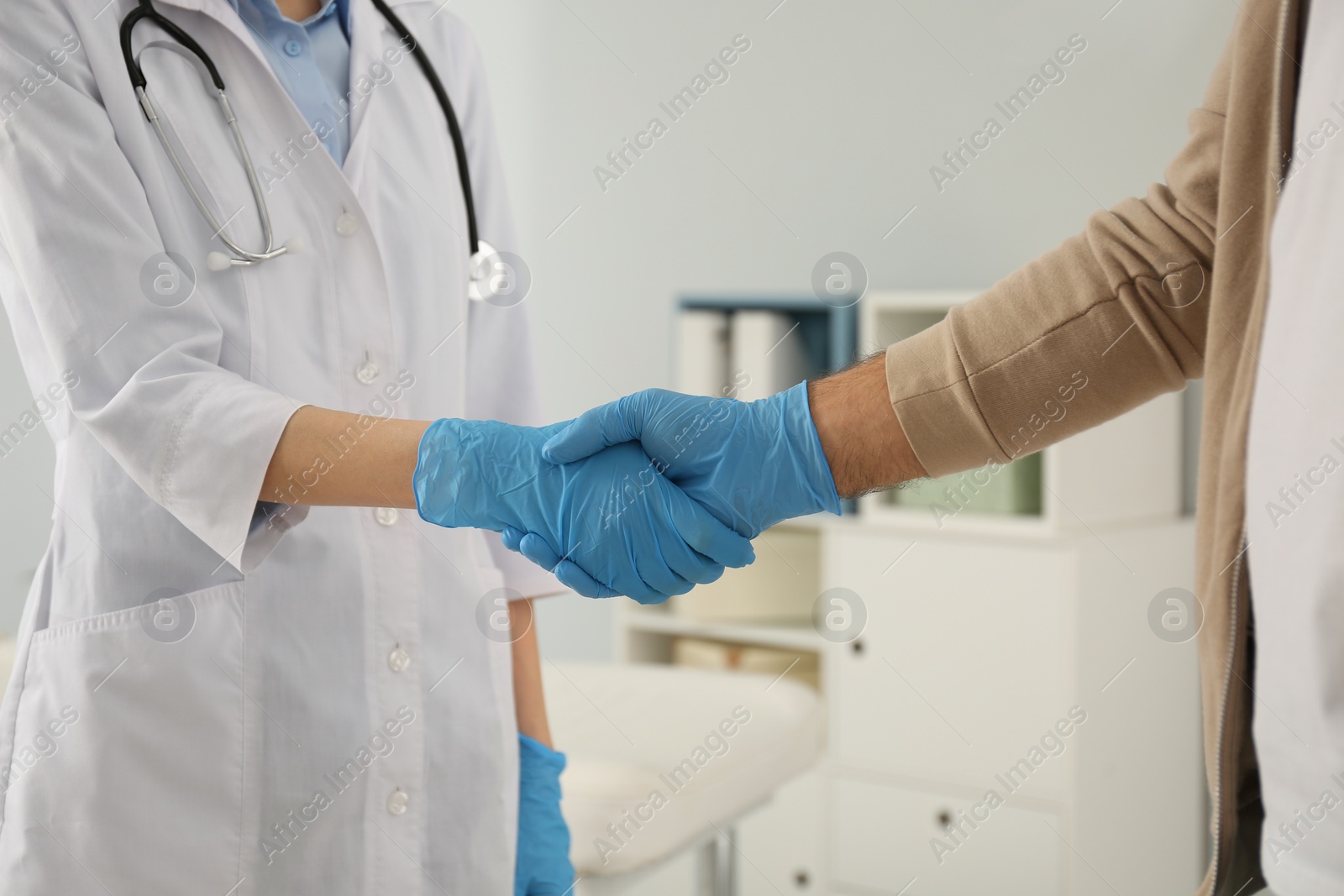 Photo of Doctor and patient in protective gloves shaking hands indoors, closeup