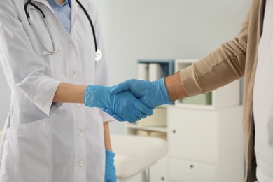 Doctor and patient in protective gloves shaking hands indoors, closeup