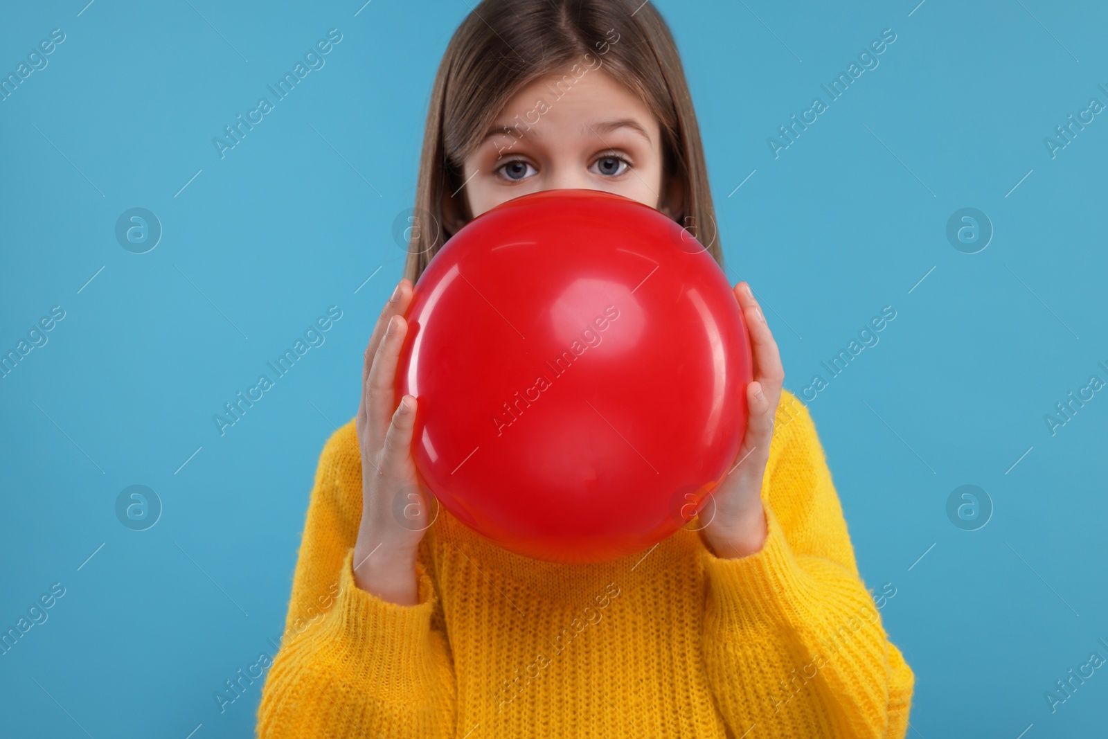 Photo of Cute girl inflating red balloon on light blue background