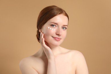 Photo of Beautiful woman with freckles and cream on her face against beige background