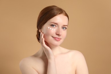 Beautiful woman with freckles and cream on her face against beige background