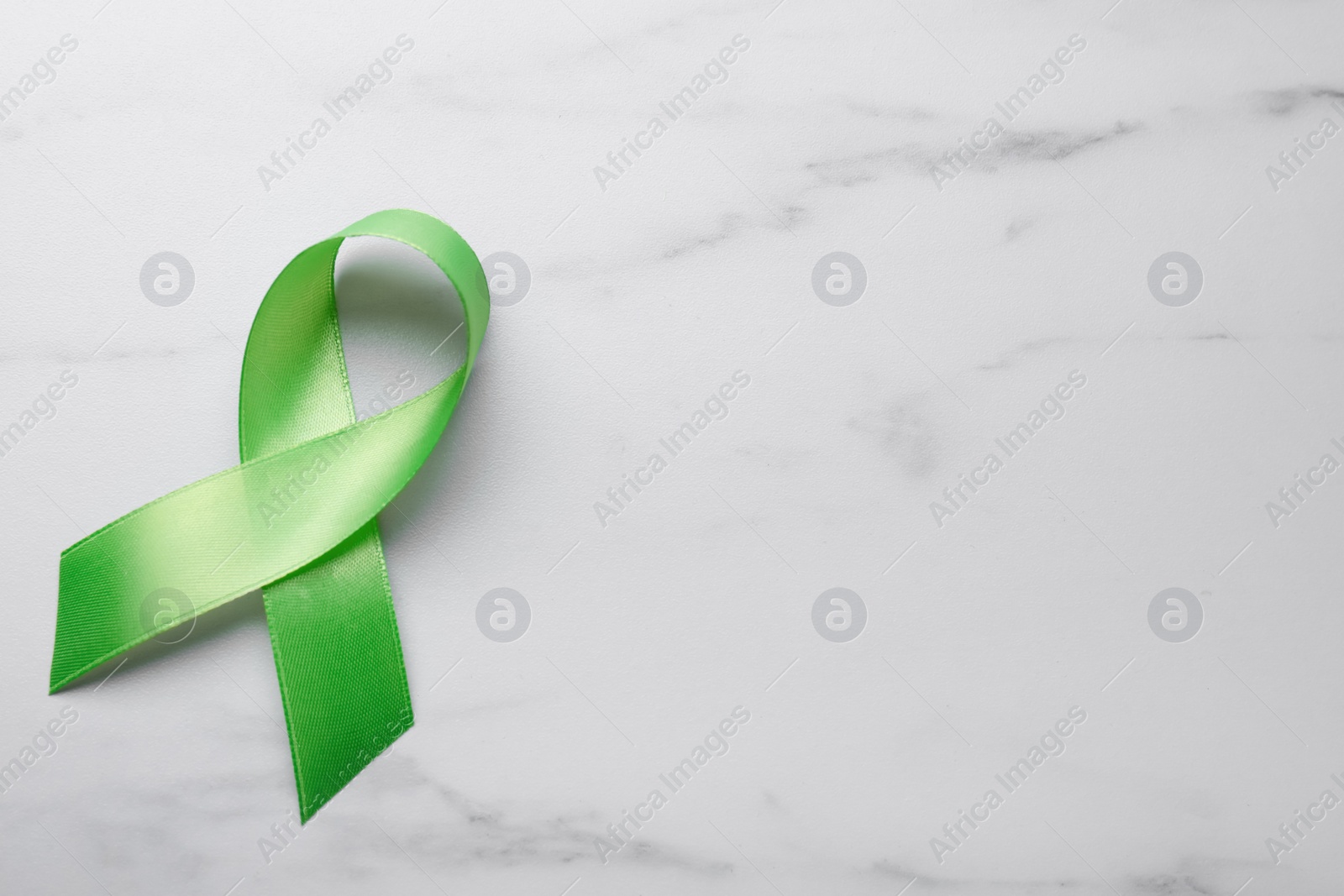 Photo of World Mental Health Day. Green ribbon on white marble table, top view with space for text