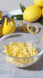 Bowl with peel pieces, fresh lemons and zester on grey table, closeup