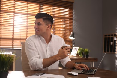 Photo of Freelancer with cup of coffee working on laptop at table indoors