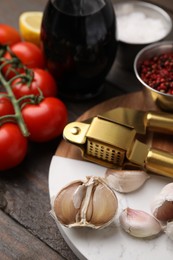 Photo of Different fresh ingredients for marinade and garlic press on wooden table, closeup