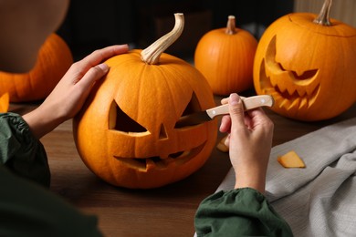 Photo of Woman carving pumpkin for Halloween at wooden table, closeup