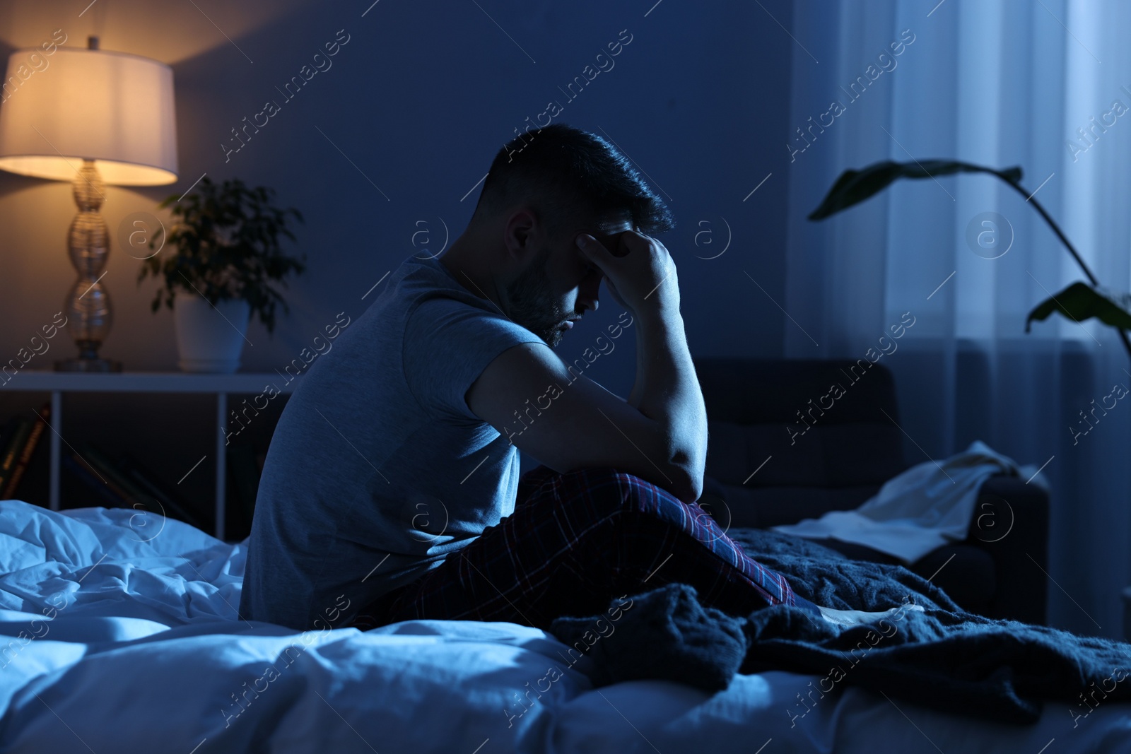 Photo of Frustrated man sitting on bed at night