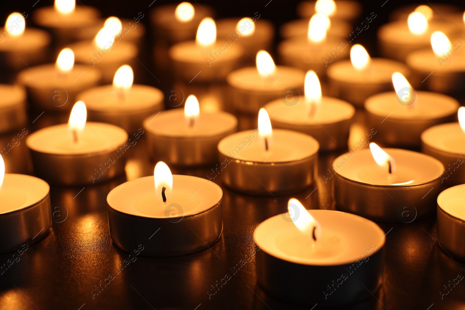 Photo of Burning tealight candles on dark surface, closeup