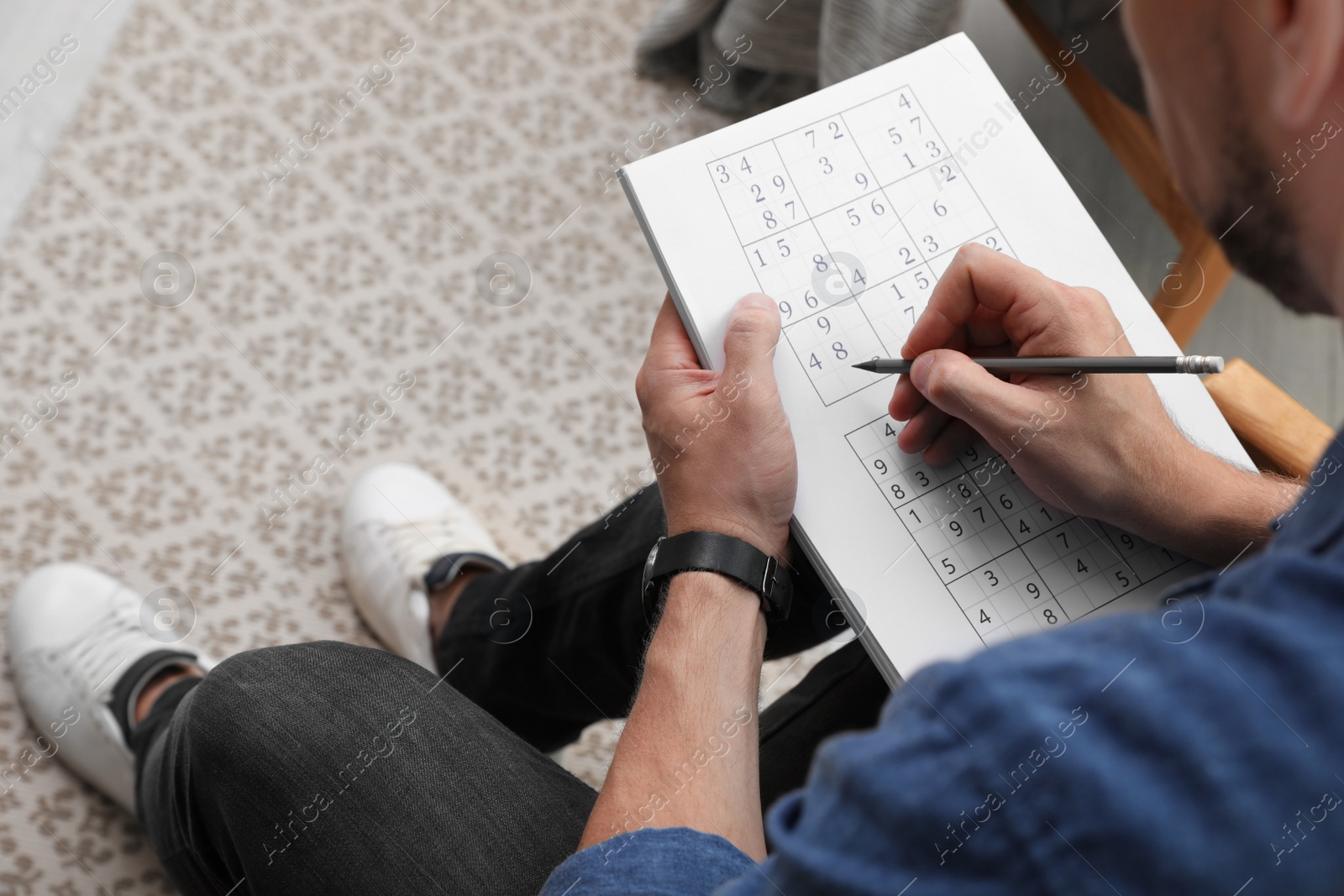 Photo of Man solving sudoku puzzle at home, closeup