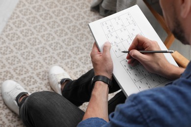 Photo of Man solving sudoku puzzle at home, closeup